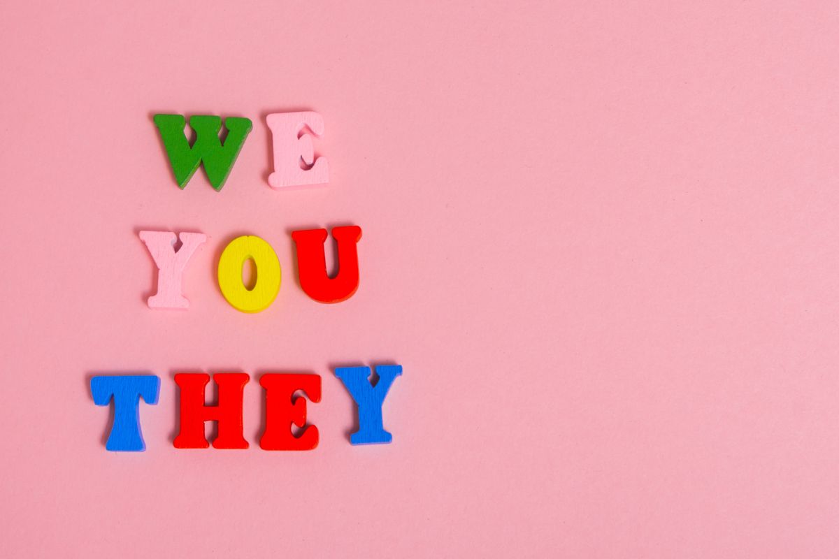 Inclusive language in policies. Colourful wooden letters on a pink background spelling out We You They. 