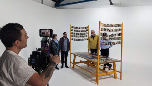 Film studio. Man behind camera and actors on a set with a large table