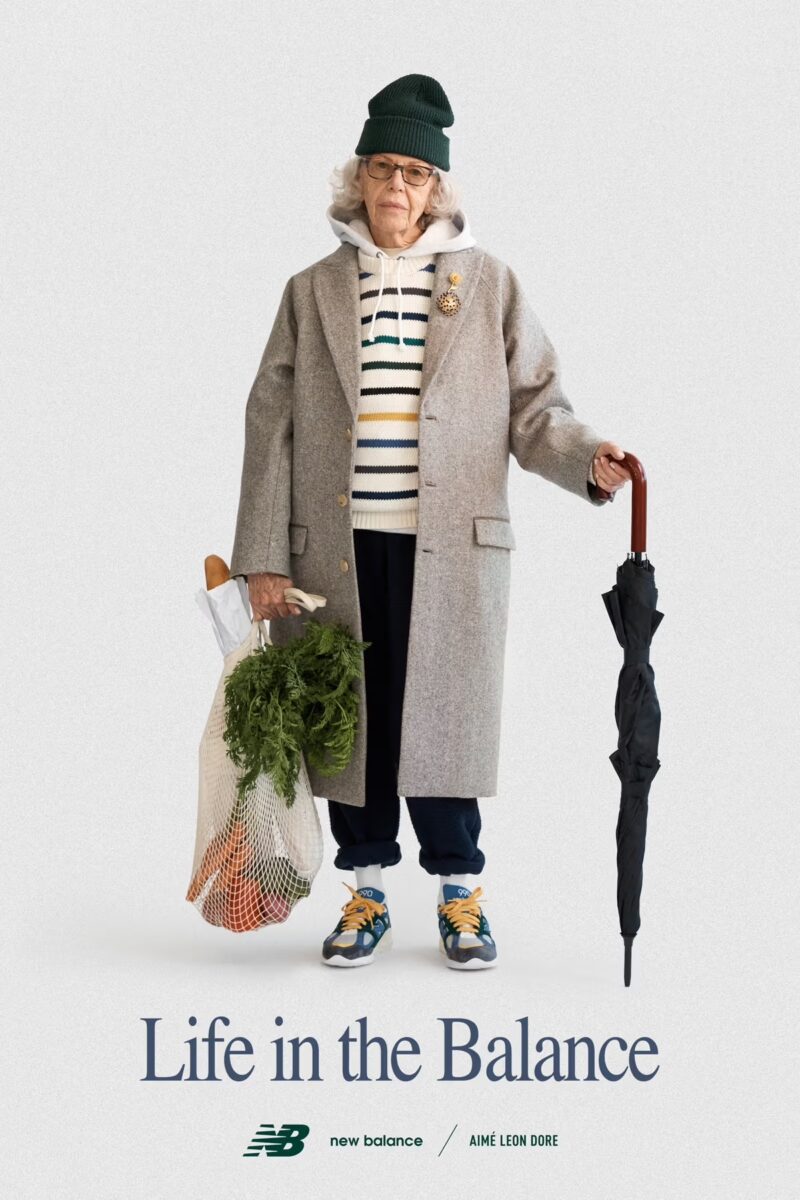 Poster from New Balance campaign showing well dressed older lady in sneakers holding a shopping bag and umbrella